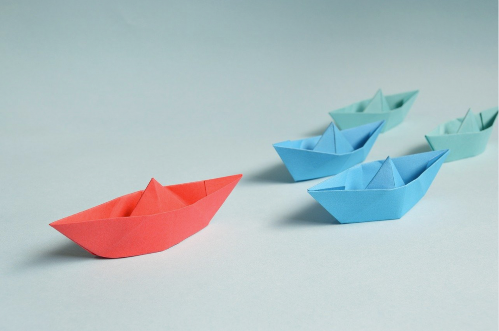 Origami paper boats in a formation with one as the leader